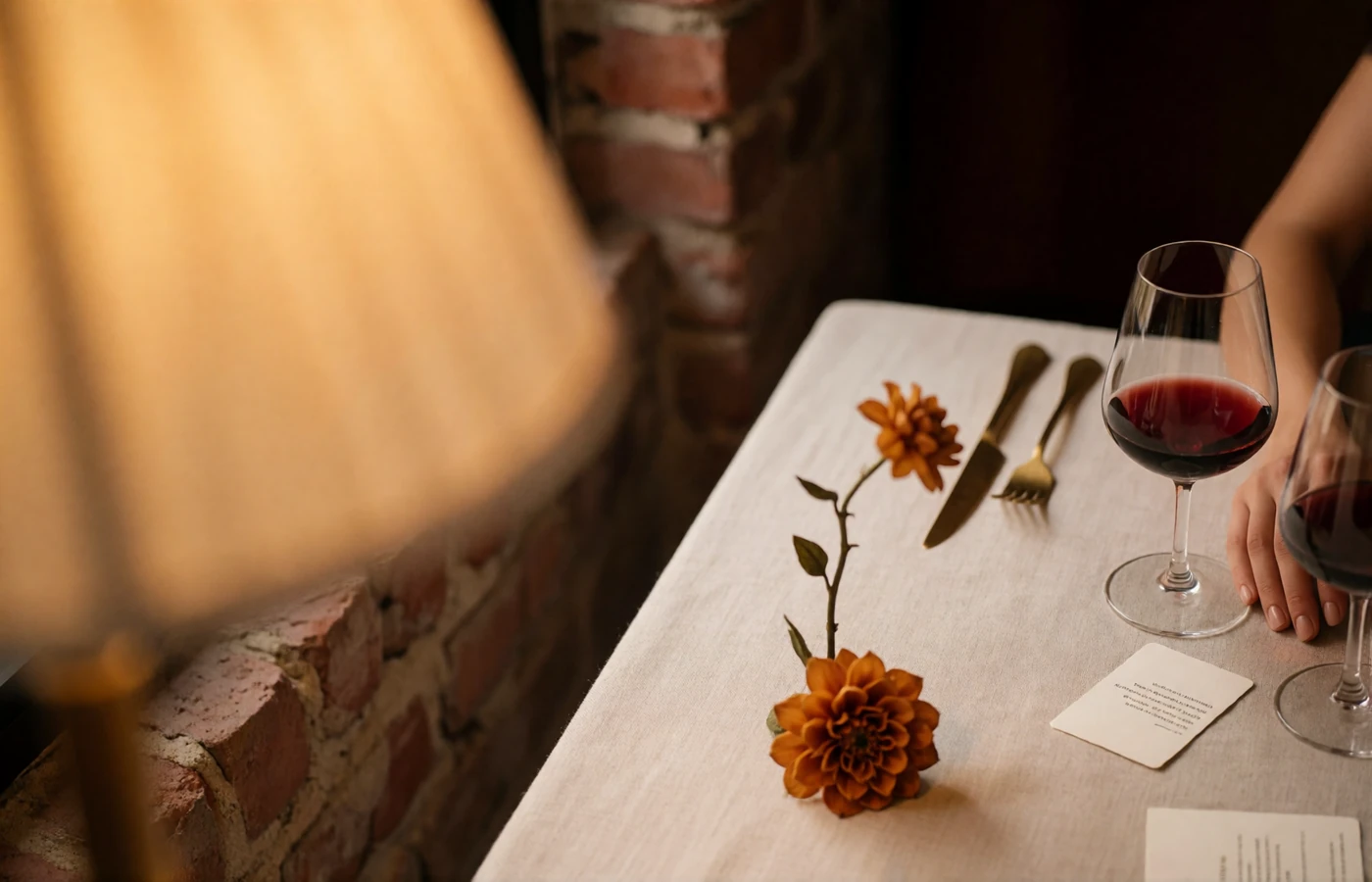 Quiet corner table set with wine glasses and a small ochre-toned floral stem in a warmly lit wine bar